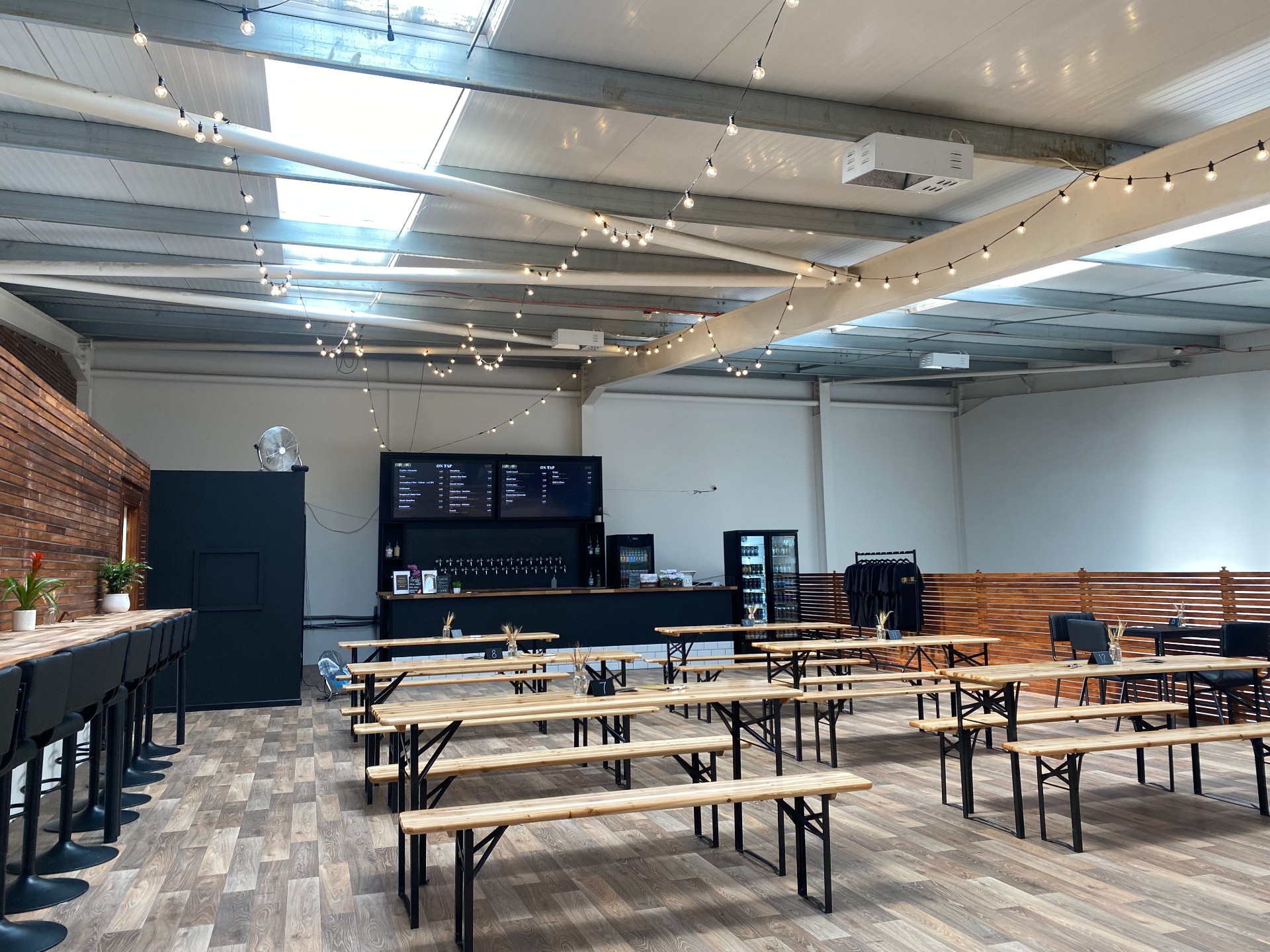 Inside the Bearwood Brewing taproom with bench seating, festoon lighting and the bar with tap list screens